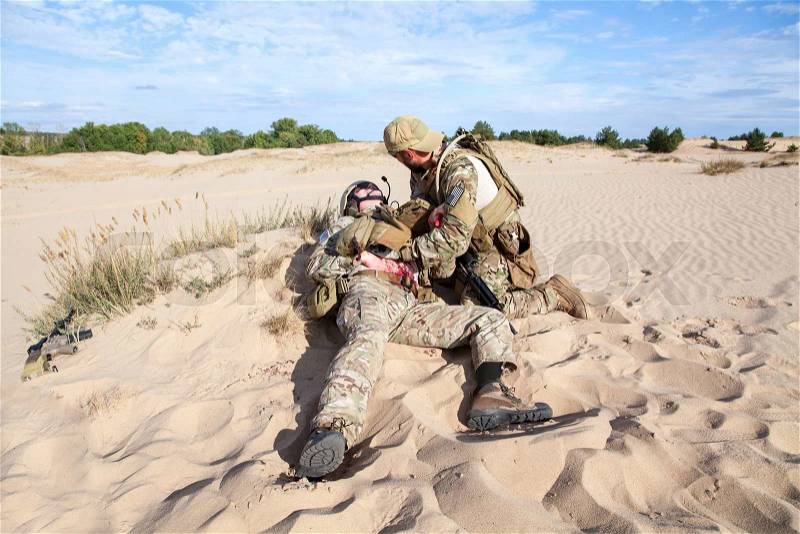 US Army Special Forces soldier medic treating the wounds of injured in the desert, stock photo