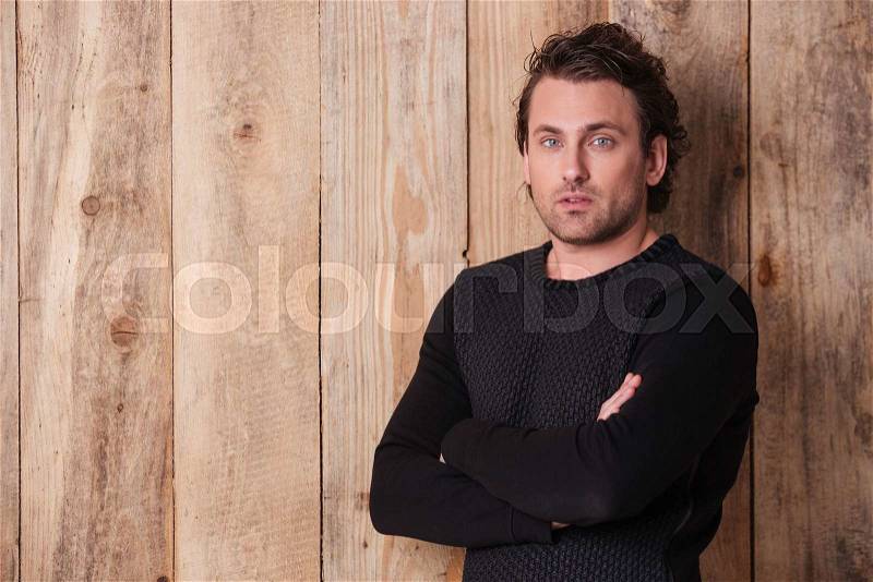Handsome curly young man in black sweater standing with arms crossed , stock photo