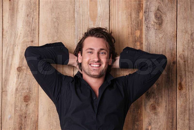 Happy relaxed young man in black shirt posing with hands behind head , stock photo