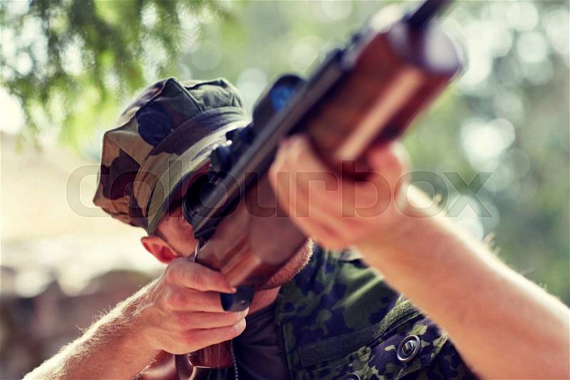 Hunting, war, army and people concept - young soldier, ranger or hunter with gun walking in forest, stock photo