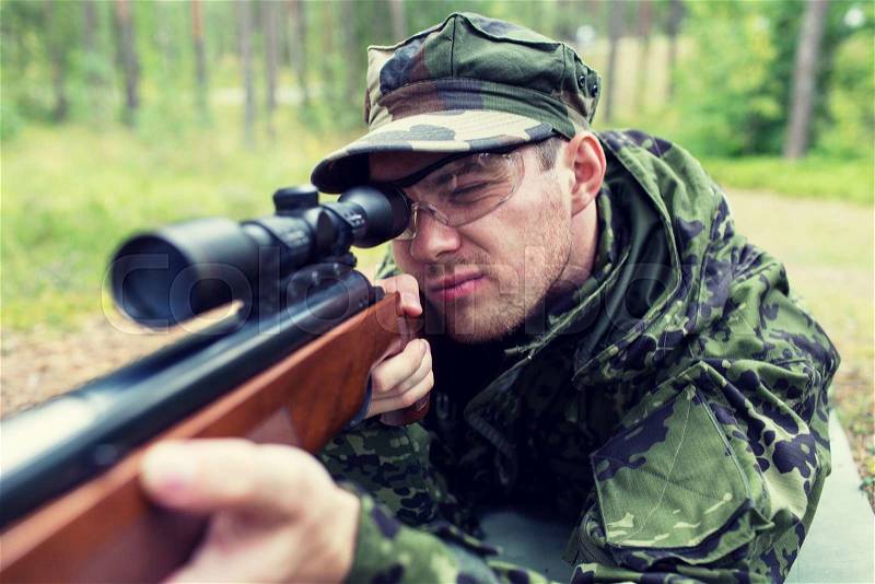 Hunting, war, army and people concept - close up of young soldier, ranger or hunter with gun in forest, stock photo