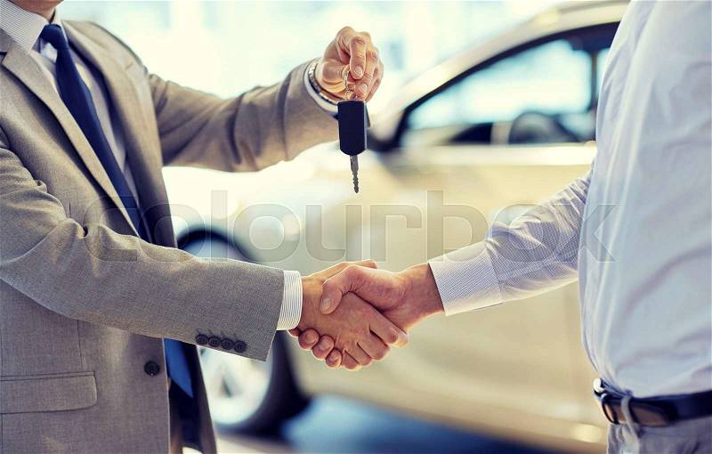 Auto business, car sale, deal, gesture and people concept - close up of dealer giving key to new owner and shaking hands in auto show or salon, stock photo