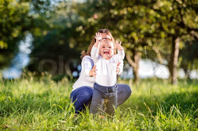 Mother holding her little son making first steps outside in green sunny nature, stock photo