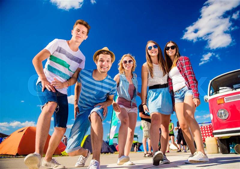 Group of teenage boys and girls at summer music festival posing by vintage red campervan, stock photo