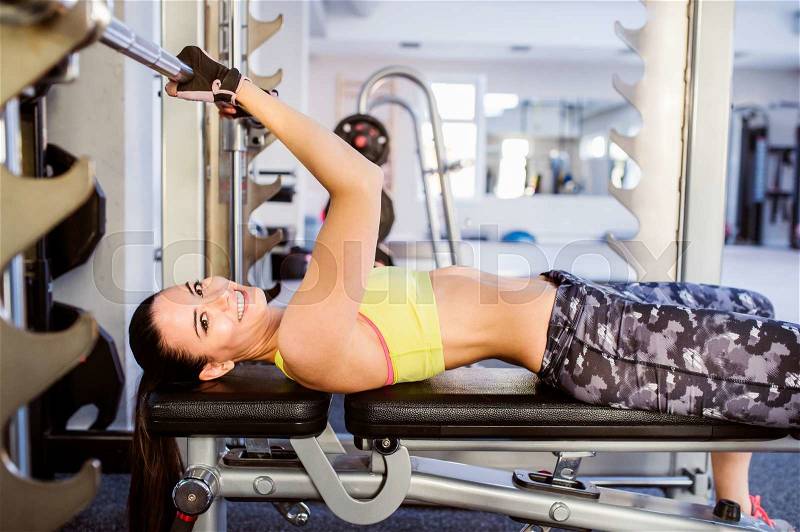 Woman in a gym working out with weights, bench pressing, stock photo