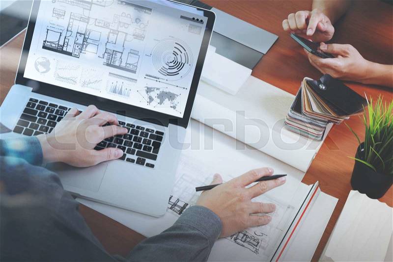 Top view of two colleagues interior designers discussing data with new modern computer laptop and pro digital tablet with sample material on wooden desk as concept, stock photo