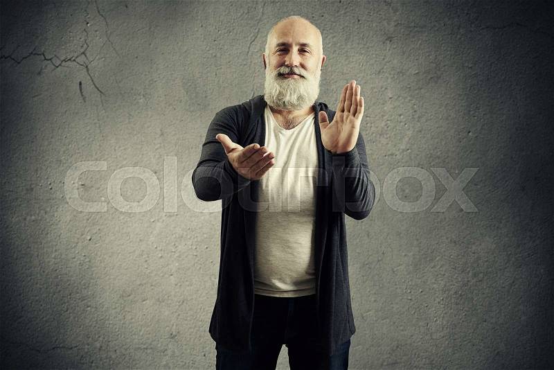 Smiley bearded man clapping and looking at camera over dark background, stock photo
