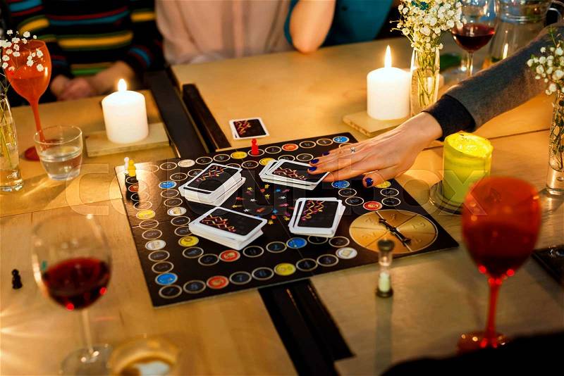 Group of people gathered to play Alias game. Young people hanging out together around a table during a party playing a game. Selective focus, stock photo