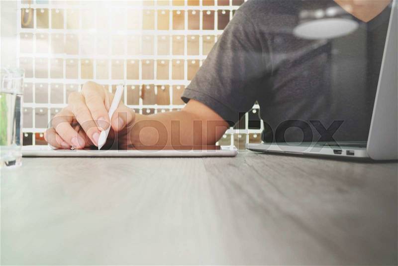 Interior designer hand working with digital tablet and laptop computer and sample material on wooden desk as concept, stock photo