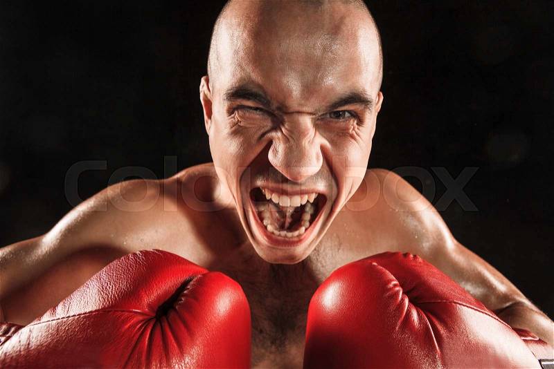 The young male athlete kickboxing on a black background with screaming face. concept fury in the fight, stock photo
