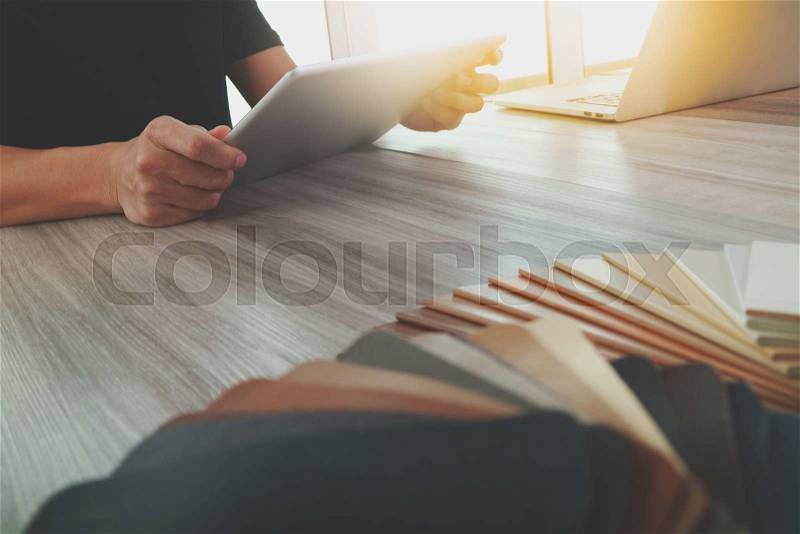 Interior designer hand working with new modern computer laptop and pro digital tablet with sample material board and digital design diagram layer on wooden desk as concept, stock photo