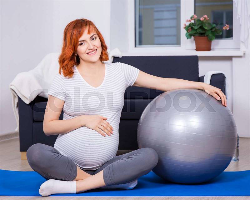 Young pretty pregnant woman exercising with fitness ball at home, stock photo