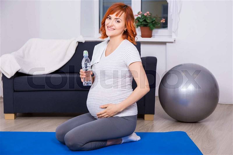 Young happy pregnant woman relaxing after fitness training at home, stock photo
