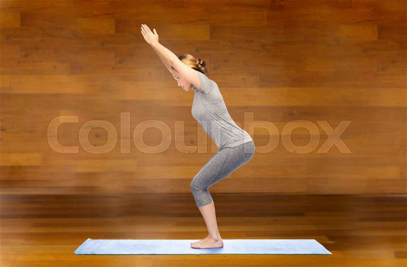 Fitness, sport, people and healthy lifestyle concept - woman making yoga in chair pose on mat over wooden room background, stock photo