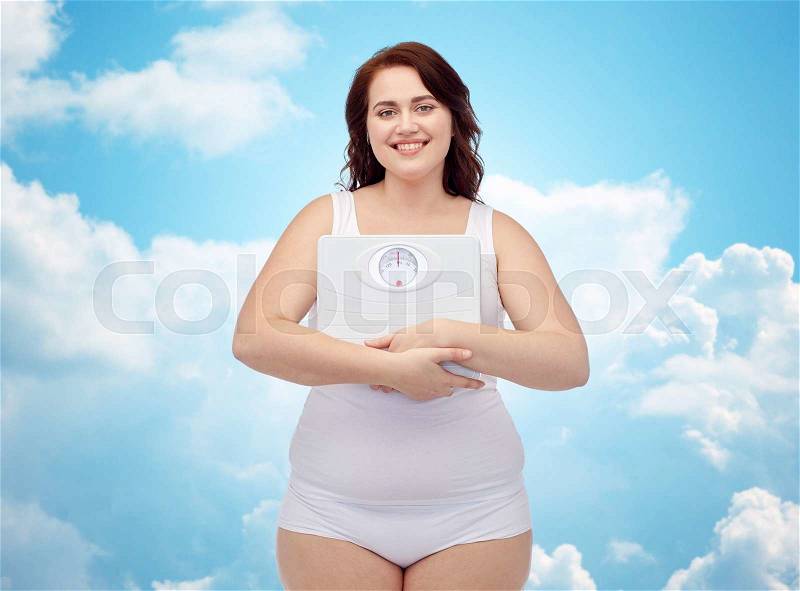 Weight loss, diet, slimming, plus size and people concept - happy young plus size woman in underwear holding scales over blue sky and clouds background, stock photo