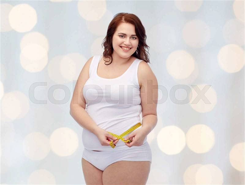 Weight loss, diet, slimming, size and people concept - happy young plus size woman in underwear measuring tape over holidays lights background, stock photo