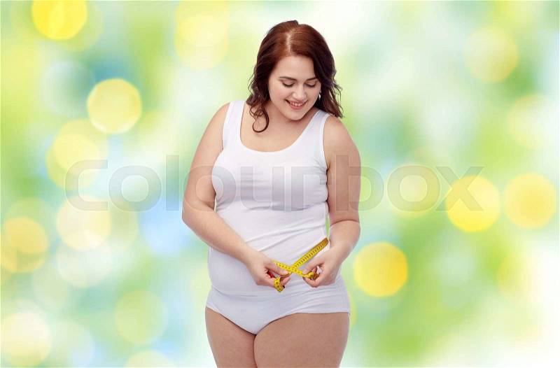 Weight loss, diet, slimming, size and people concept - happy young plus size woman in underwear measuring tape over green lights background, stock photo