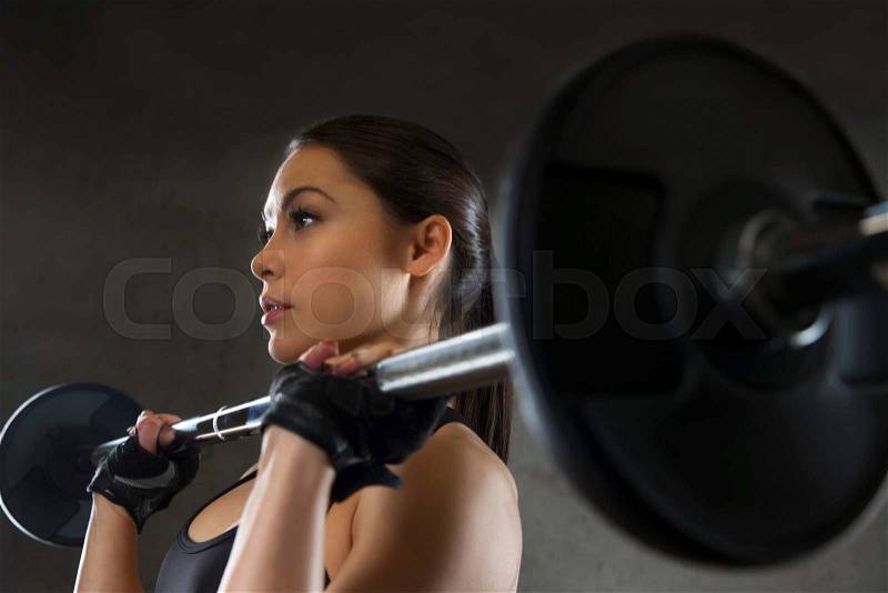 Sport, fitness, bodybuilding, weightlifting and people concept - young woman with barbell flexing muscles in gym, stock photo
