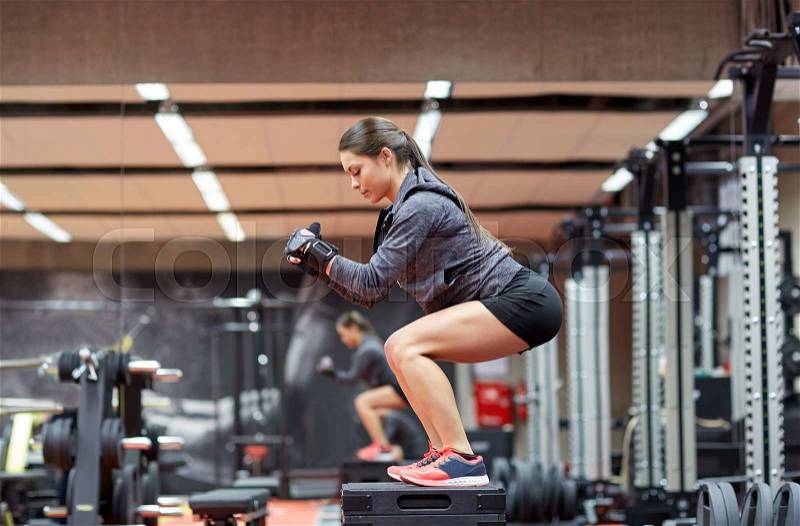 Fitness, sport, exercising and people concept - woman doing squats on platform in gym, stock photo