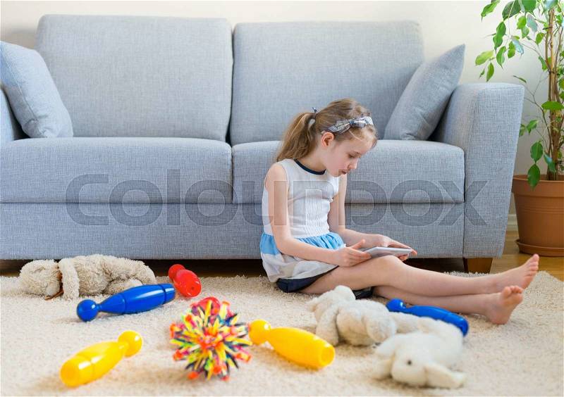 It\'s time to clean up your toys! Little girl playing with tablet pc, don\'t want to do the cleaning, stock photo