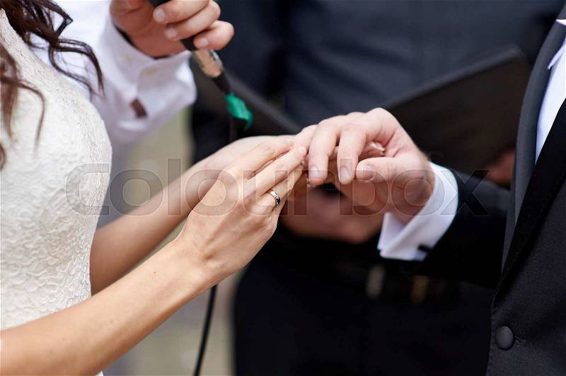 Bride wears a wedding ring on finger of groom, stock photo