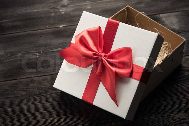 White gift box with red ribbon bow on dark wood background, stock photo