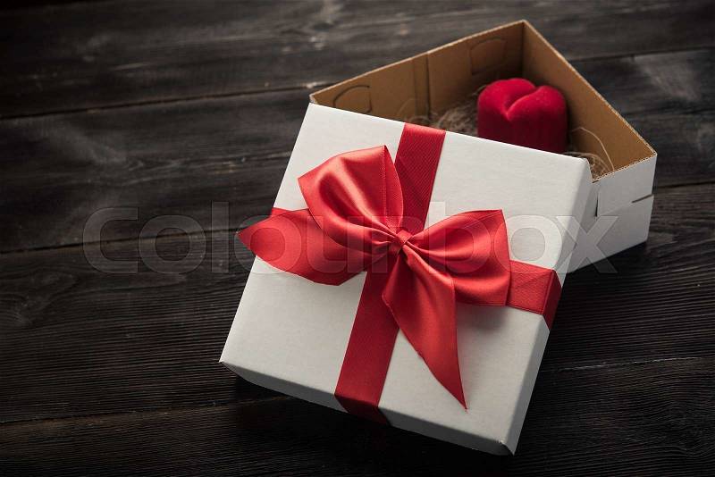 White gift box with red ribbon bow on dark wood background, stock photo