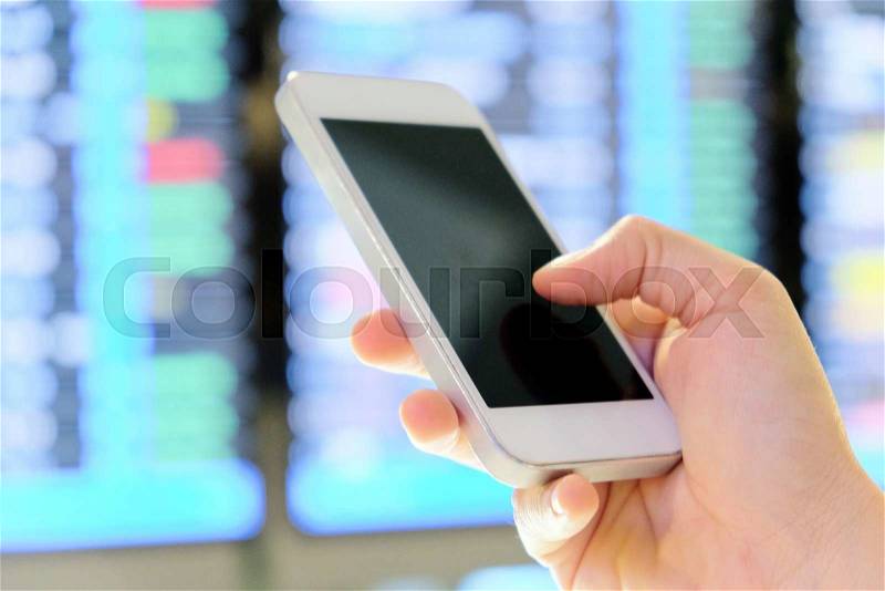 Hand holding smartphone on a flight information board in the airport background, stock photo