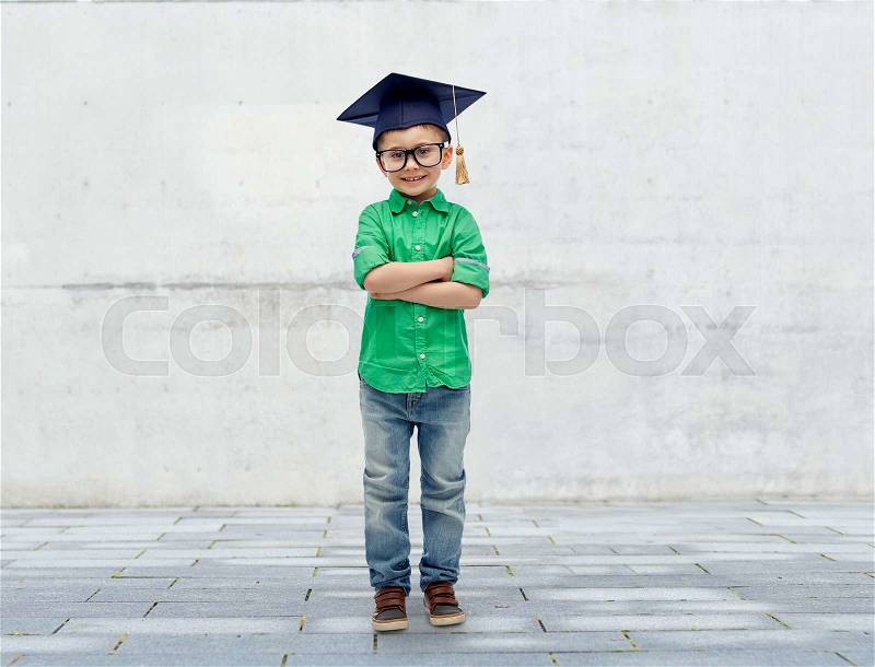 Childhood, school, education, learning and people concept - happy boy in bachelor hat or mortarboard over urban city street background, stock photo