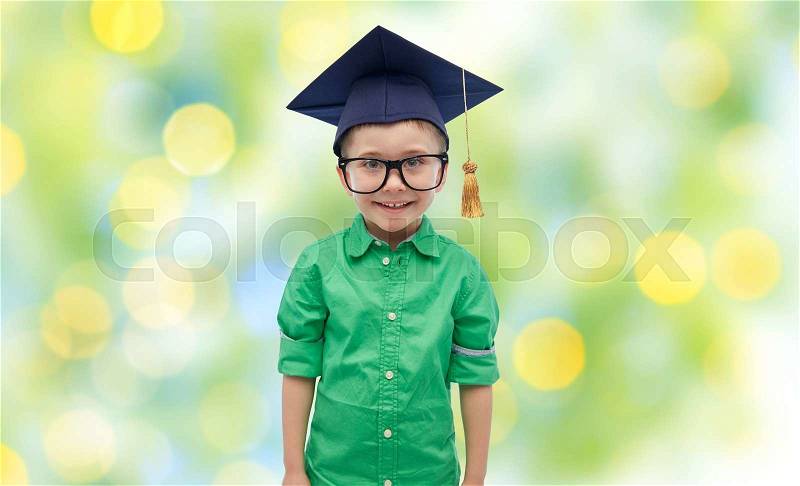 Childhood, school, education, learning and people concept - happy boy in bachelor hat or mortarboard over green lights background, stock photo
