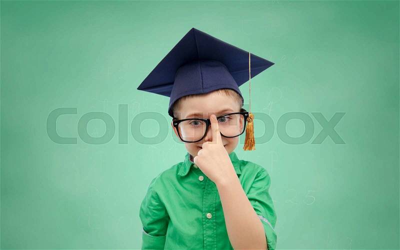 Childhood, school, education, knowledge and people concept - happy boy in bachelor hat or mortarboard and eyeglasses over green school chalk board background, stock photo