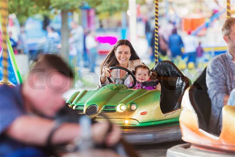Cute little girl with her mother having fun at fun fair, driving a bumper car, amusement park, stock photo