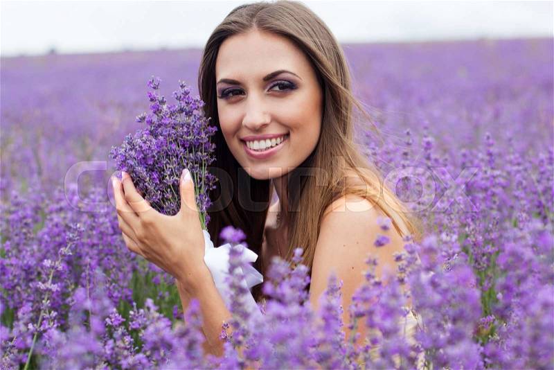 Closeup portrait of beautiful smiling girl at field of purple lavender flowers with flying hair, stock photo
