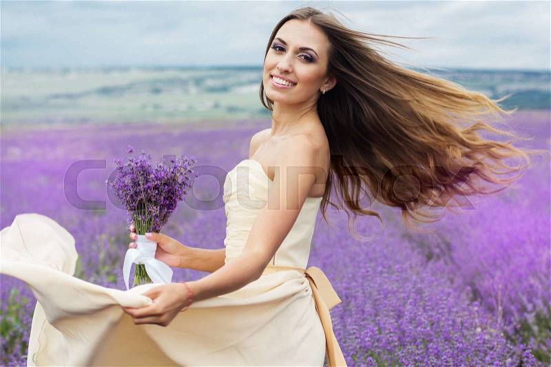 Beautiful smiling girl at field of purple lavender flowers with flying hair, stock photo