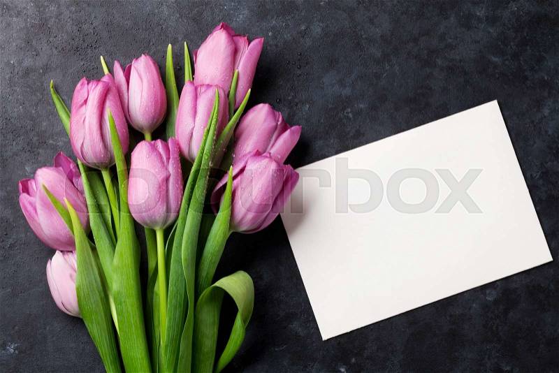 Fresh purple tulip flowers and blank greeting card on dark stone table. Top view with copy space, stock photo