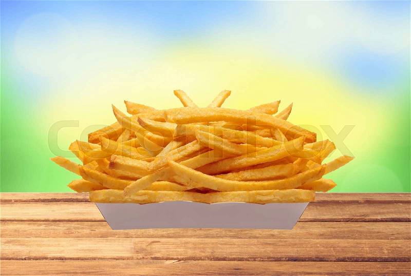 French fries in white box on table over nature background, stock photo