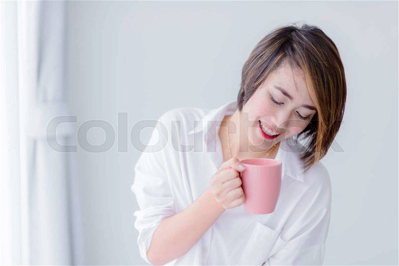 Attractive Asian woman holding coffee mug and relaxing at home. Lifestyle concept, stock photo