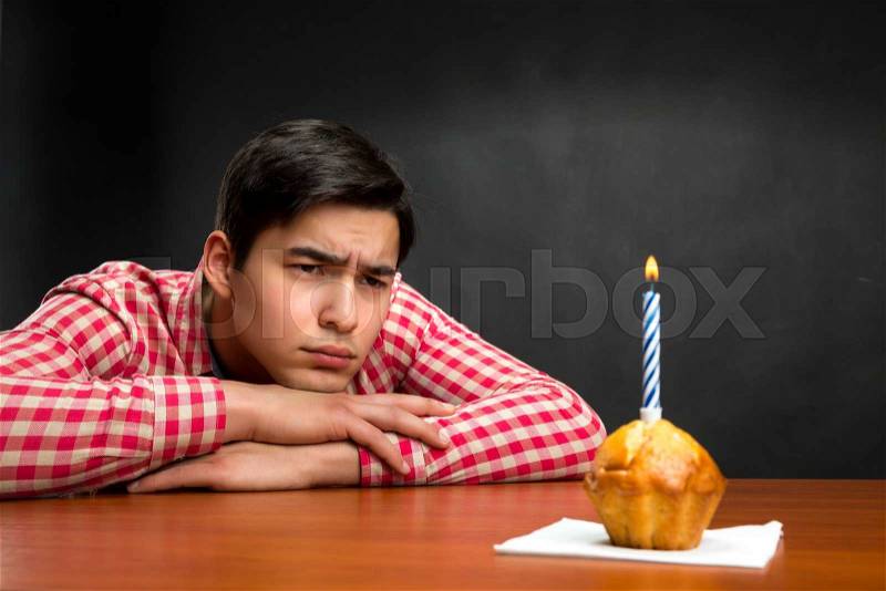 Sad birthday boy and a small cupcake with candle at the table, stock photo