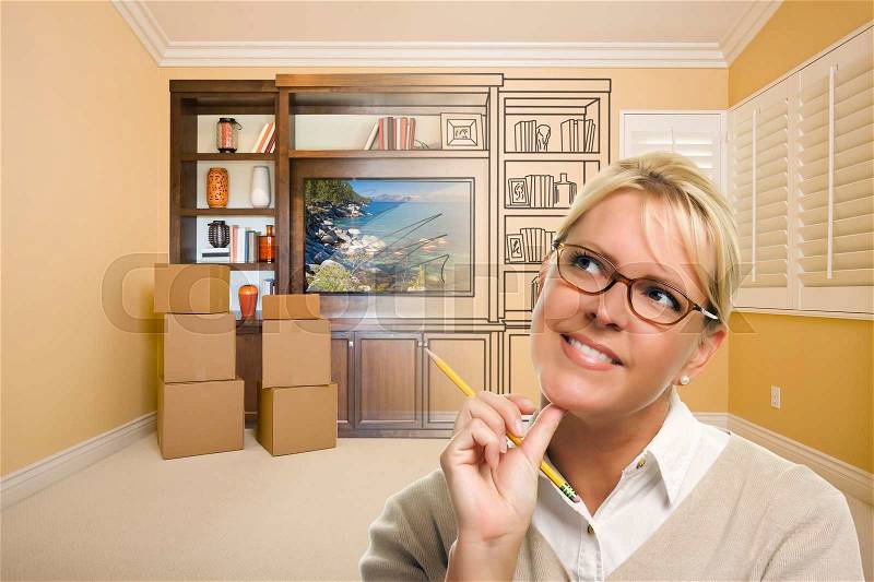 Female Holding Pencil In Room With Moving Boxes and Drawing of Entertainment Unit On Wall, stock photo