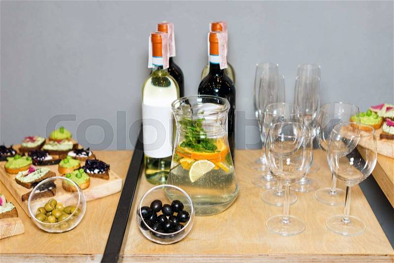 Wooden tray of appetizers at a banquet on a decorated tea table with red and white wine and carafe of fruity beverage with mint and lemon. Beautifully decorated table set in the restaurant, stock photo
