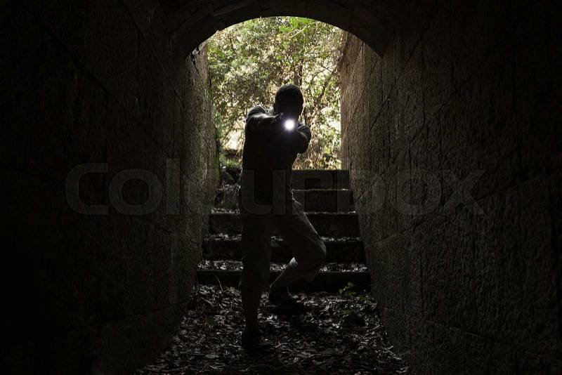 Scared young man with a flashlight enters the stone tunnel and looks in the dark, tonal correction photo filter effect, stock photo