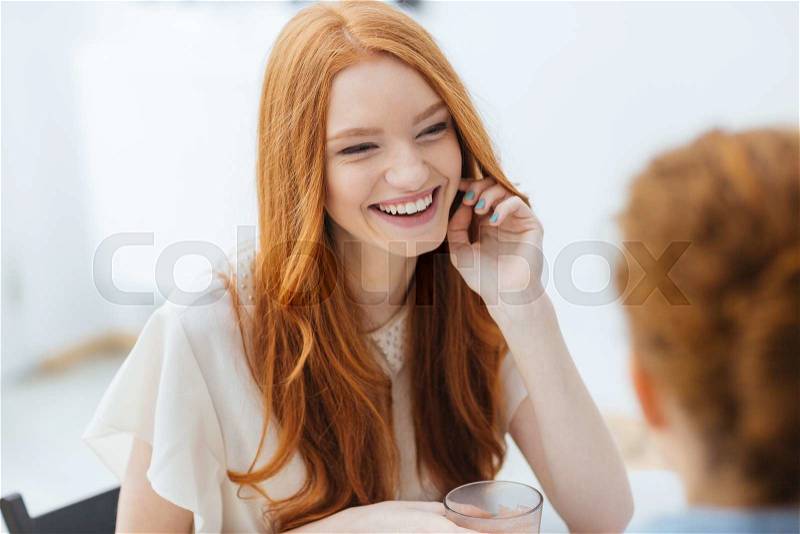 Cheerful redhead pretty young woman sitting and laughing with friend in cafe, stock photo
