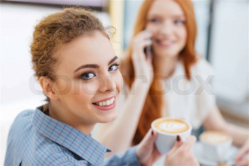 Happy cute young woman drinking coffee with her friend in cafe , stock photo