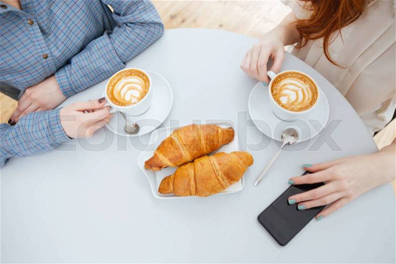 Top view of two women drinking coffee with croissants on white round table , stock photo