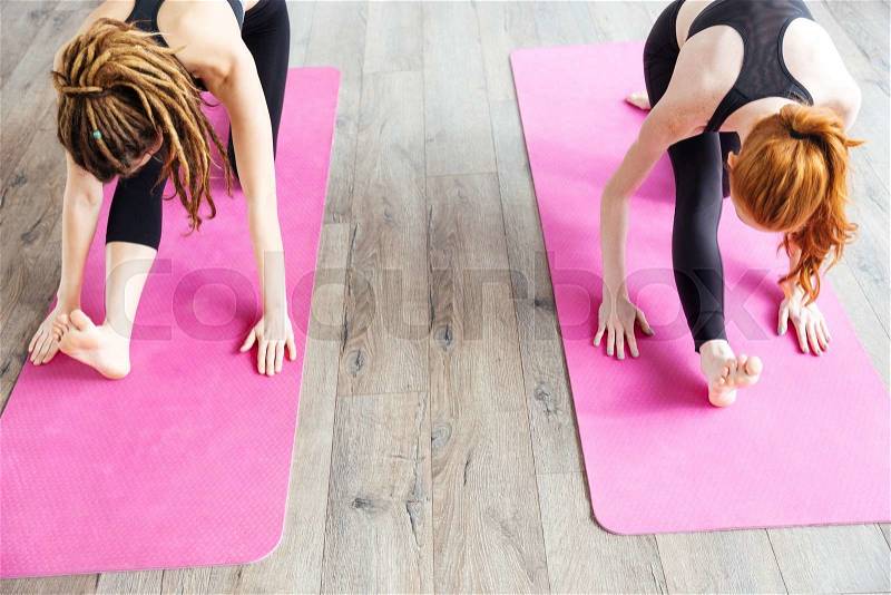 Top view of two slim young women stretching legs on pink yoga mat , stock photo