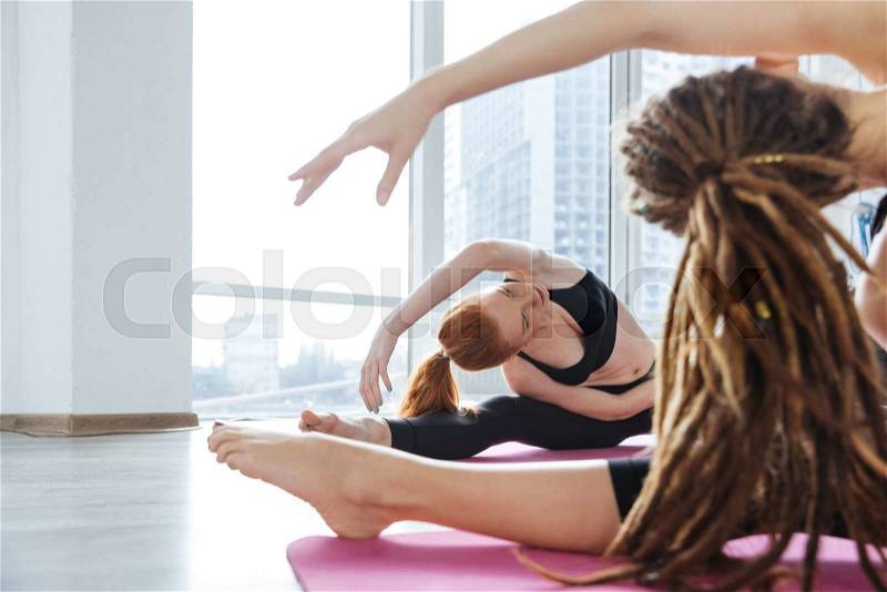 Two cute young woman stretching on the floor in yoga center together, stock photo