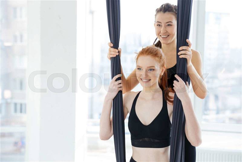 Smiling cute redhead young woman doing antigravity yoga in studio, stock photo