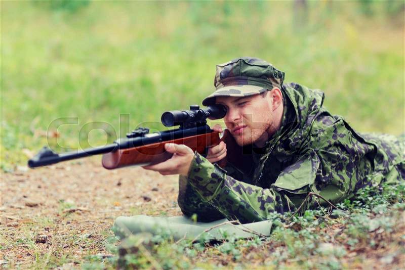 Hunting, war, army and people concept - young soldier, ranger or hunter with gun aiming and shooting in forest, stock photo