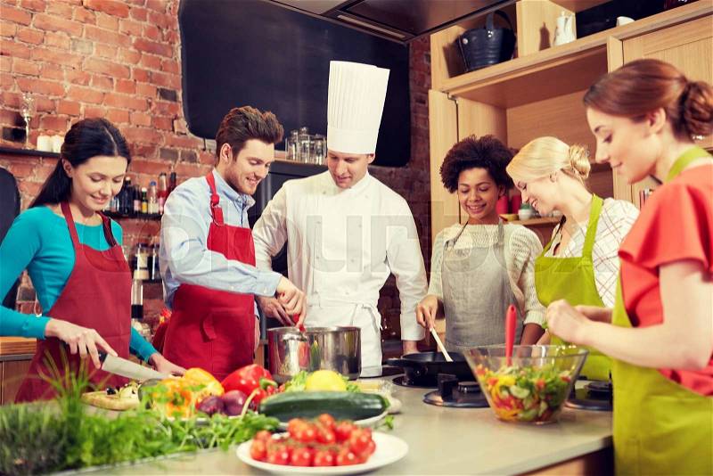 Cooking class, culinary, food and people concept - happy group of friends and male chef cook cooking in kitchen, stock photo