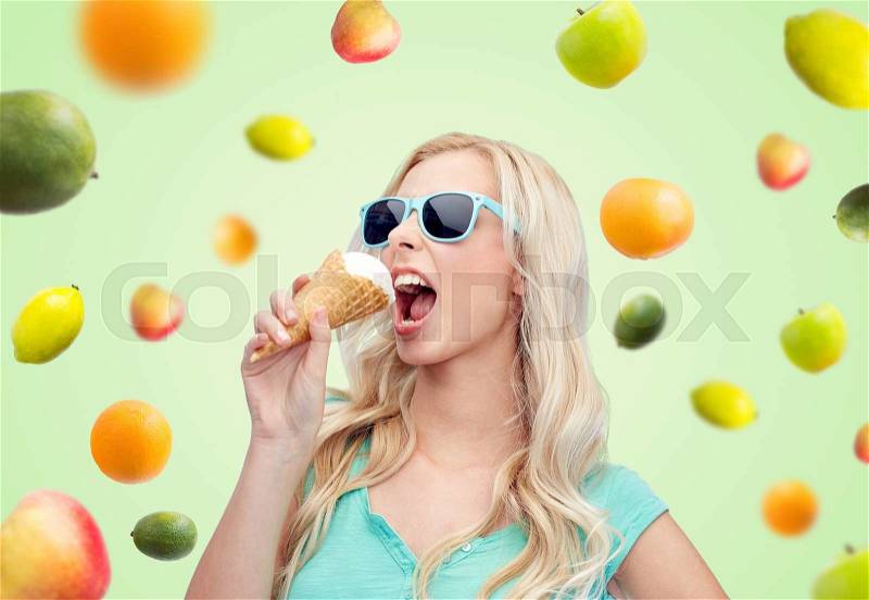Summer, junk food and people concept - young woman or teenage girl in sunglasses eating ice cream over green natural background with fruits, stock photo